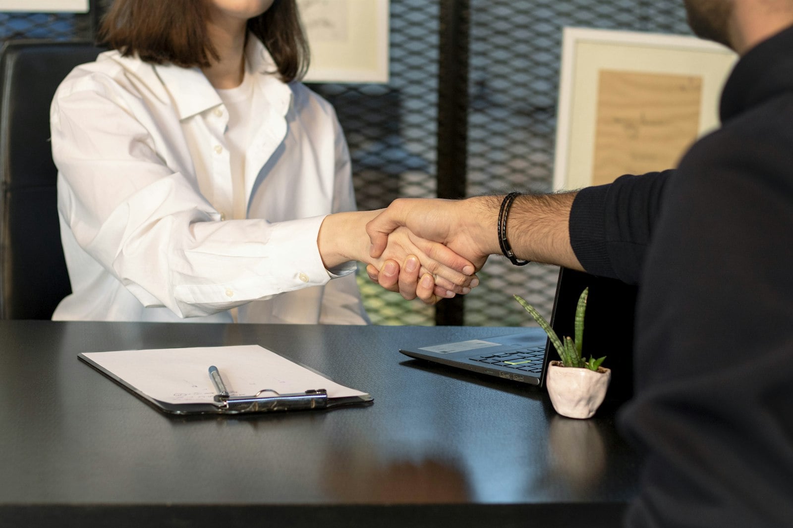 new home care marketing liaison shaking hands with a manager during onboarding, laptop and clipboard on the desk